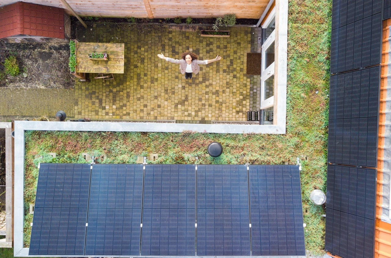 Foto met drone, bovenaf, dakbedekking groen, met zonnepanelen, vrouw in beeld met armen gespreid