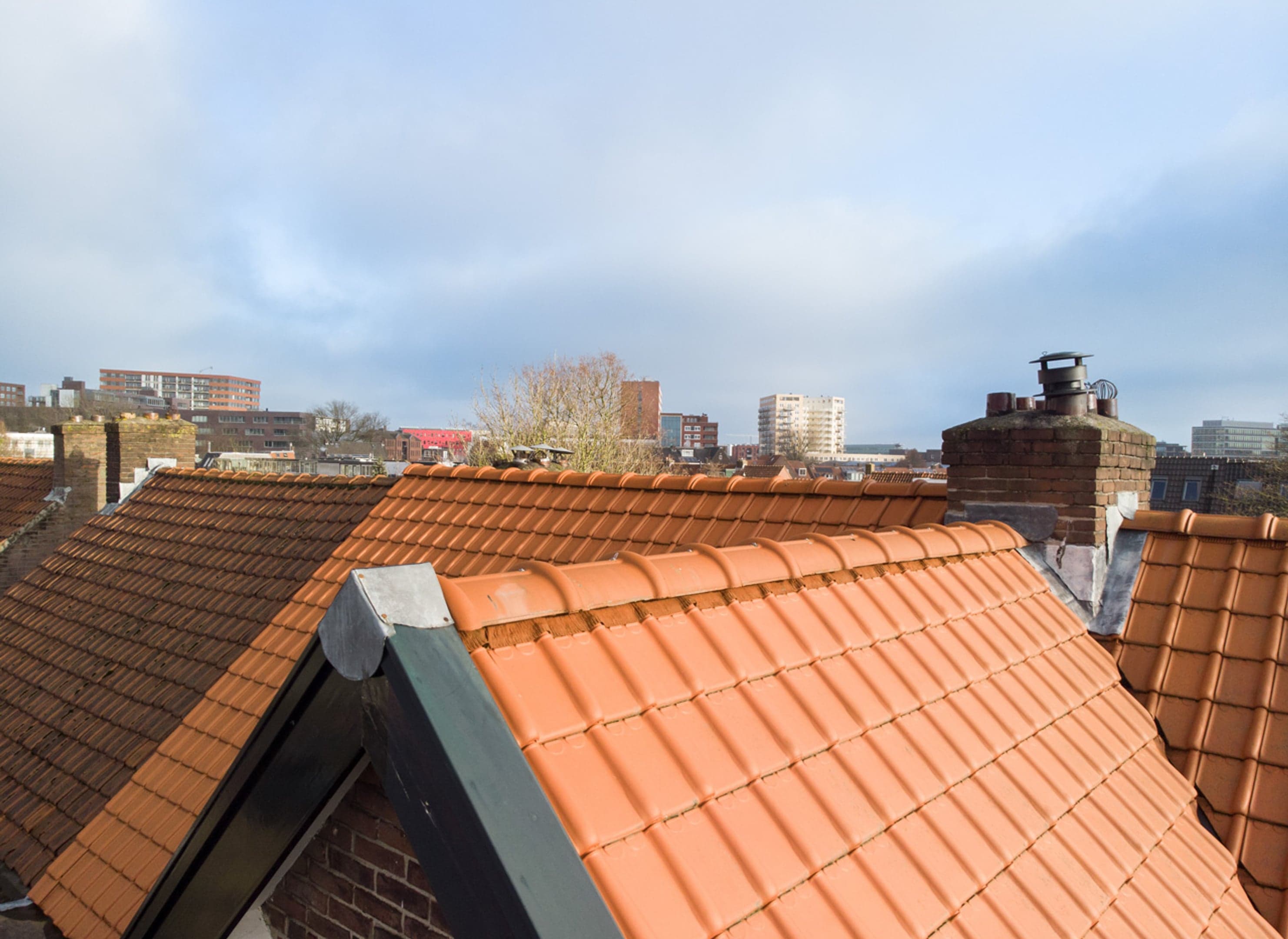 Dak van een oudere woning met nieuwe dakpannen, uitzicht over de daken in de rest van de wijk